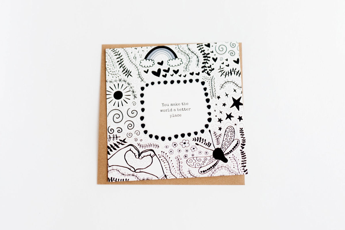 A square greeting card featuring black doodle-style illustrations of suns, rainbows, plants, and butterflies, and the text 'You make the world a better place'. The card is laying on a brown kraft envelope, on a white background.