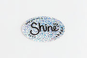 An oval sticker with a holographic glitter background and the word 'baby girl, let it Shine' in black script, shown on a plain white background.