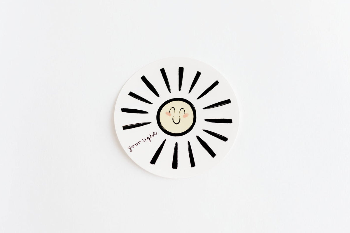 A round white sticker featuring a doodle sun design with a smiley face in the center, shown on a clean white background.